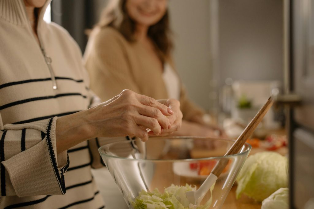 Close-up of hands preparing a fresh salad in a glass bowl within a cozy kitchen atmosphere.